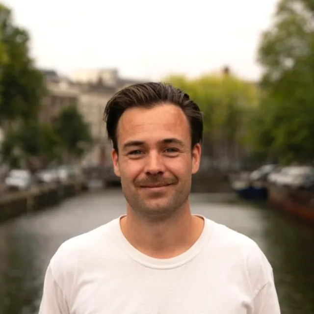 Thomas Lock, glimlachend in een wit T-shirt langs een Amsterdamse gracht